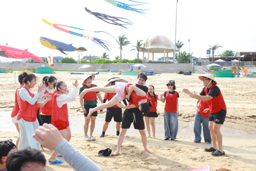 Đội áo đỏ chơi trò kéo đẩy đồng đội trên bãi cát trong team building