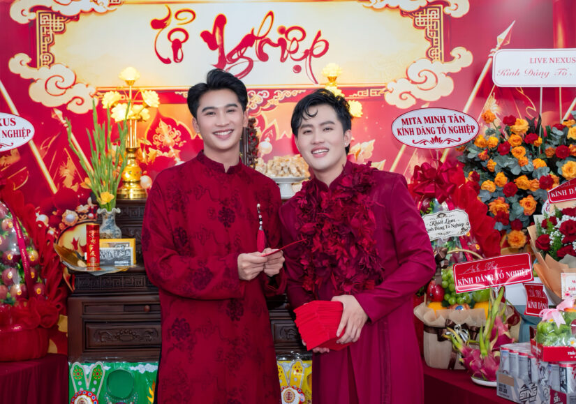 Hai thành viên mặc áo dài đỏ cầm phong bao đứng trước bàn thờ Tổ nghiệp