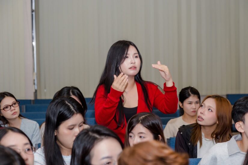 Học viên ngồi hàng ghế hội trường giơ tay phát biểu trong workshop về giọng nói