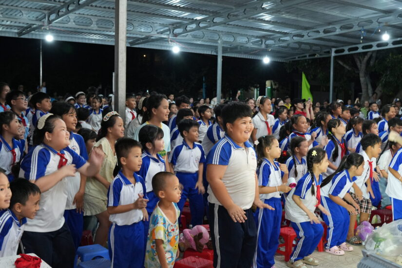 Các em học sinh ngồi xem văn nghệ đêm trung thu, tay ôm phần quà được tặng