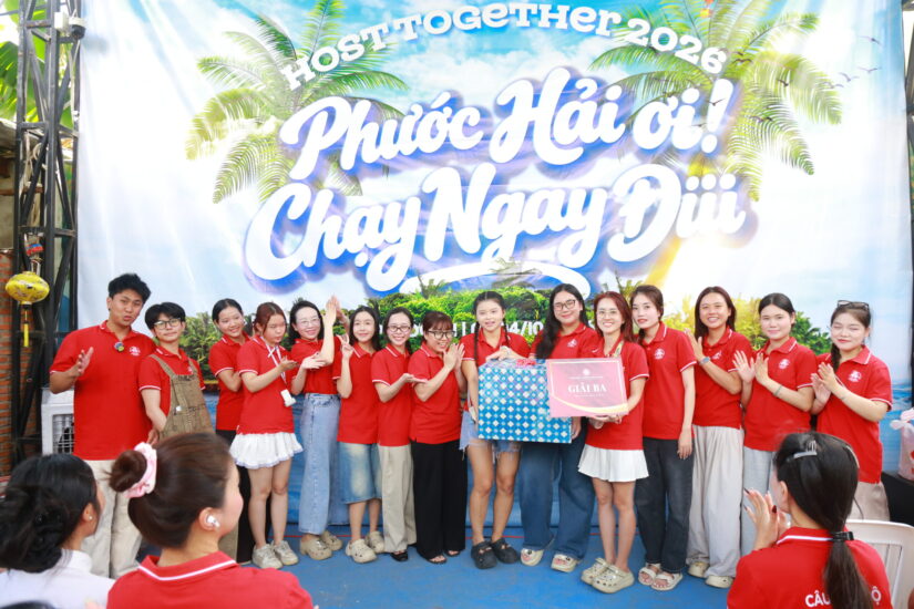 Thành viên CLB áo đỏ chụp ảnh chung với tấm bảng quà tặng trước phông nền Host together 2026
